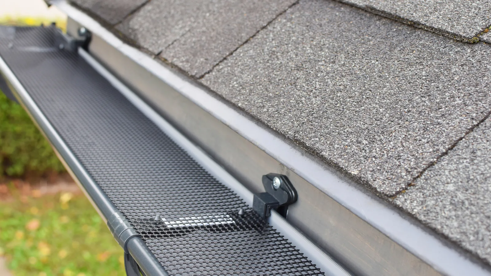 Mesh gutter guard fastened along the edge of an asphalt shingle roof